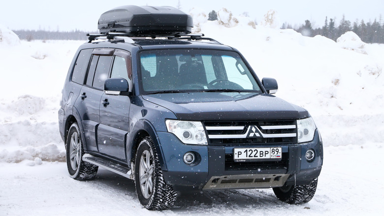A dark blue Mitsubishi Pajero with a roof box in the snow, front 3/4 view