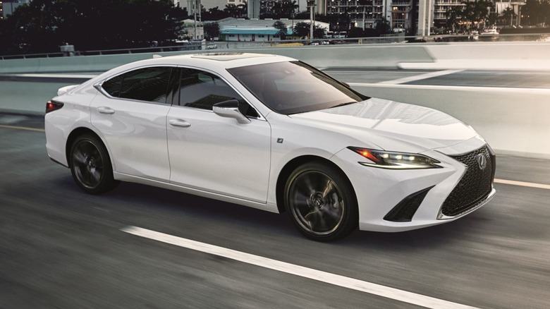 2025 Lexus ES 350 driving down a road with buildings in the background