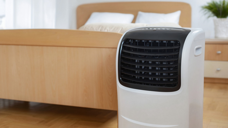 A portable air conditioner sitting at the foot of a bed in a modern room