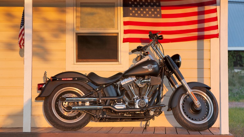 Black Harley-Davidson Fat Boy parked on a porch, with an American flag hanging behind it