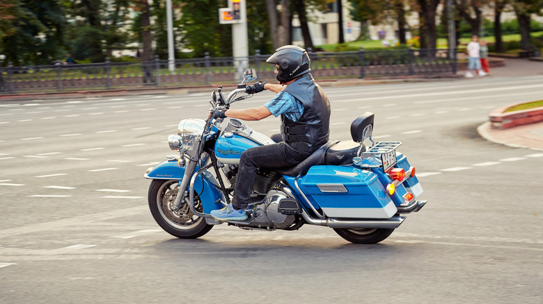 Man making a left turn through an intersection riding a blue Harley Davidson Road King