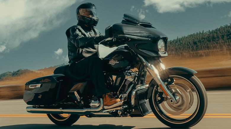 A biker dressed in a black leather jacket and helmet riding a black Street Glide