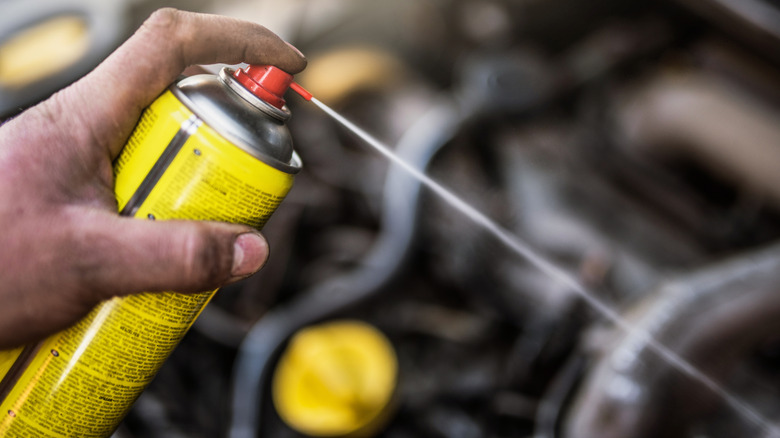 Hand holding a spray can and spraying a car engine