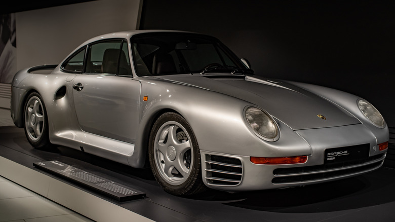 A silver Porsche 959 on display in a museum, front right 3/4 view