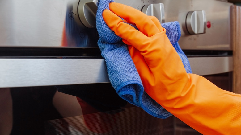 A close-up of a gloved person's hand cleaning an oven with blue cloth