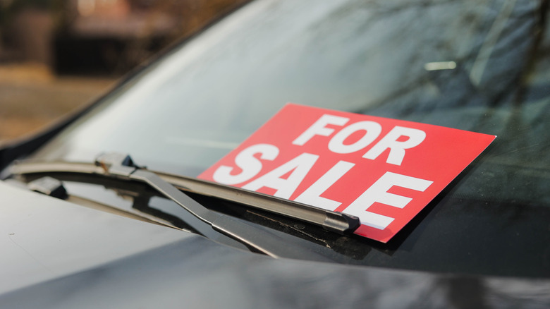Close up of a car dashboard with a red For Sale card underneath the front windscreen wipers.