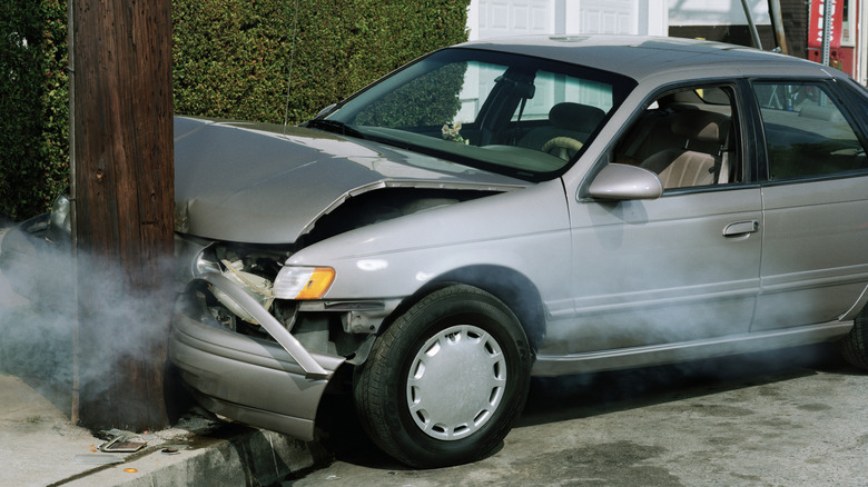 A side view of a gray car that has driven into a post