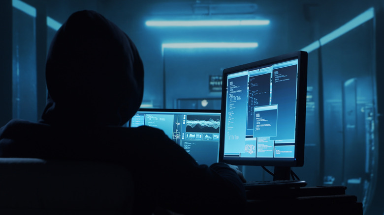 Computer hacker wearing a hoodie looking at computer screens