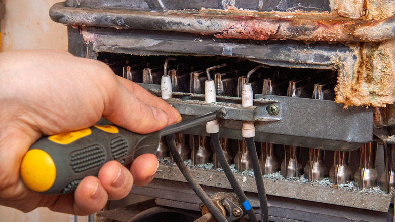 person holding a screw driver to inspect and repair a gas water heater