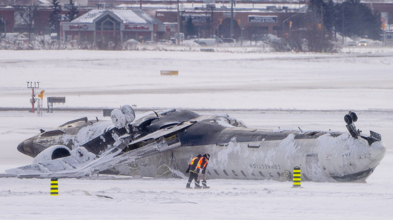 Delta flight 4819 lies upside down in the snow as airport workers inspect the wreckage