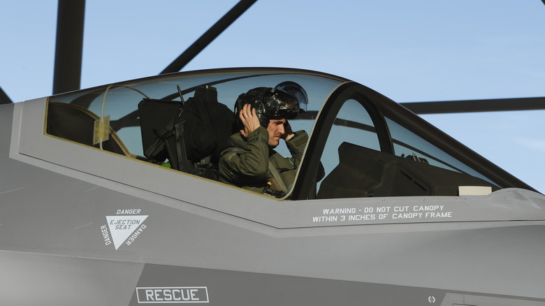 An F-35 pilot prepares for a mission by putting on his helmet in the cockpit