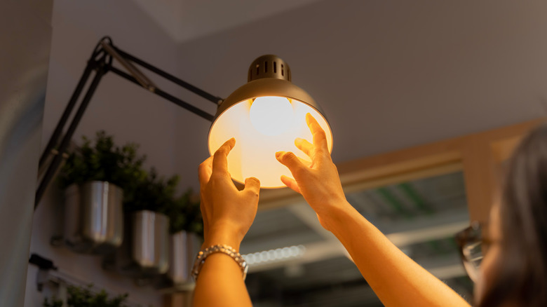 A person reaching for a warm LED bulb in a lamp.