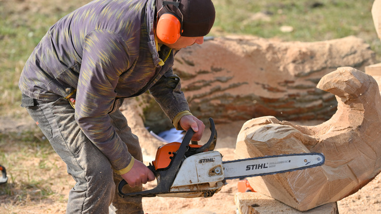 A man wearing headphones carving wood with Stihl chainsaw
