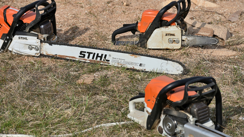 Three Stihl chainsaws with orange handle kept on ground