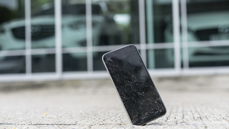 A phone dropped on the ground, with a cracked front surface.