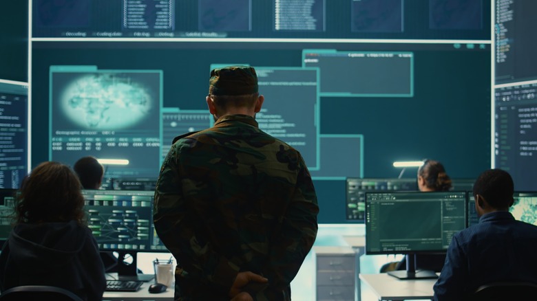Dramatic scene of a uniformed military official standing in a room full of military hackers and displays