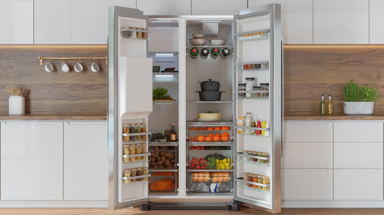 A fully-loaded refrigerator with its doors open in the middle of a kitchen.