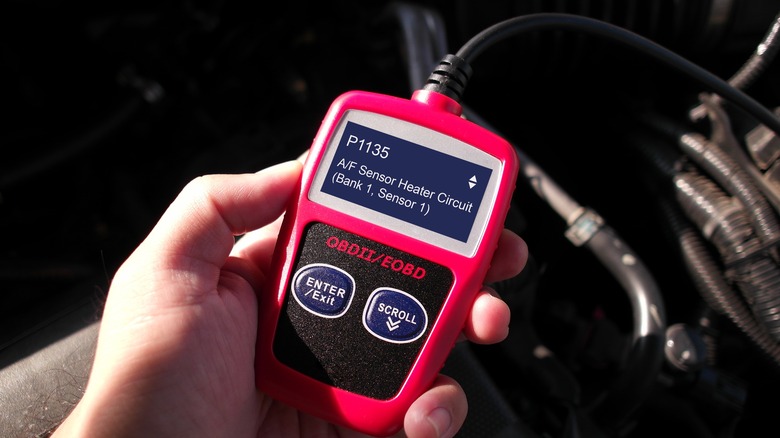 Hand holding red OBD scanner plugged into car
