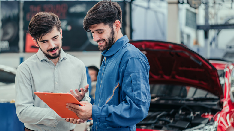 Auto mechanic and customer looking at clipboard with car in background.