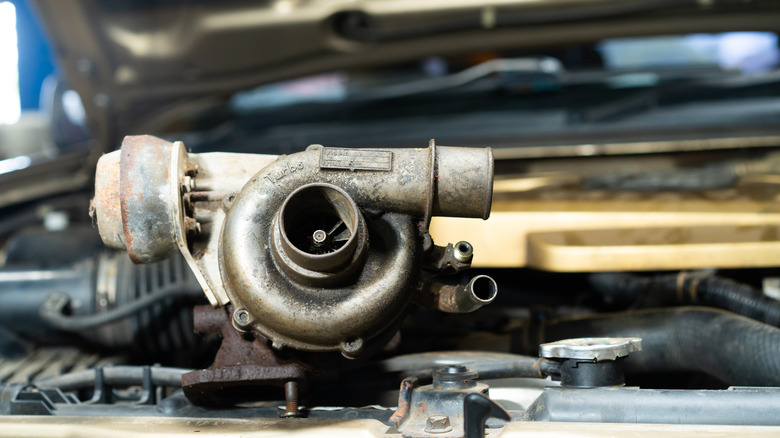 Old and worn-down turbocharger resting on top of vehicle engine.