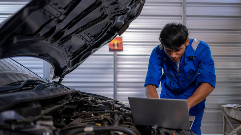 Auto mechanic checking for engine issue with laptop.