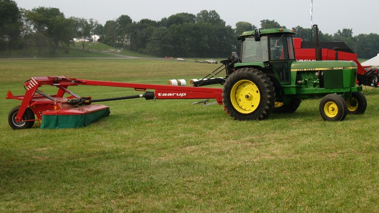 A John Deere tractor pulling a large PTO-driven mower.