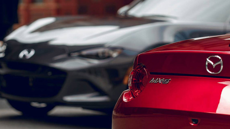 Close-up of a Miata's rear badge, with another Miata in the background
