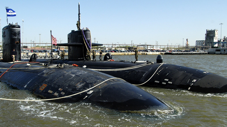 Two black colored submarines partially submerged, side-by-side, docked.