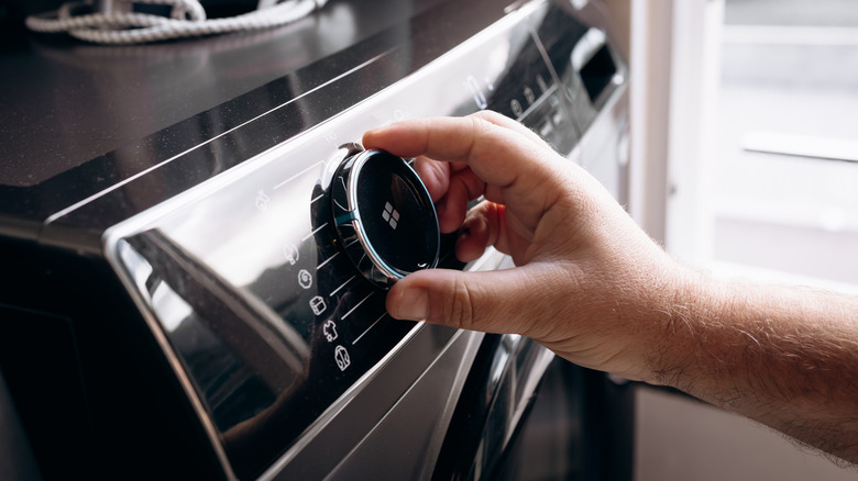 A hand is turning the control dial on a modern washing machine