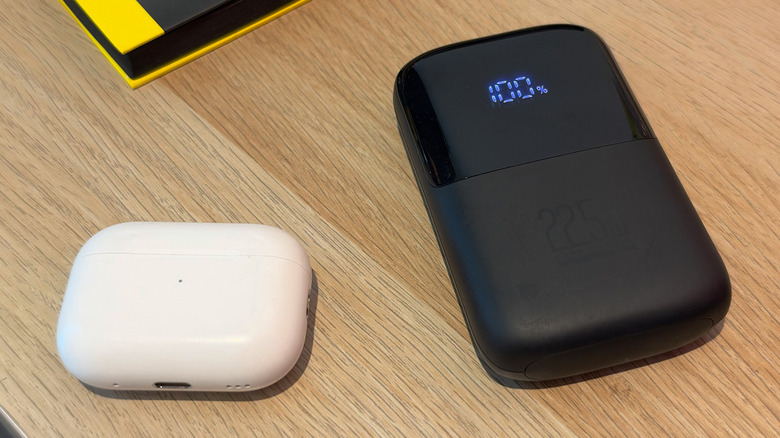 A power bank next to an AirPods case on a wood table.