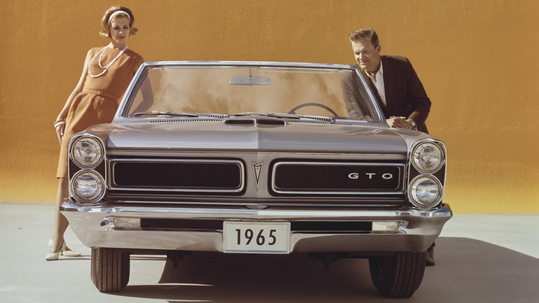 Man and woman standing next to 1965 Pontiac GTO convertible