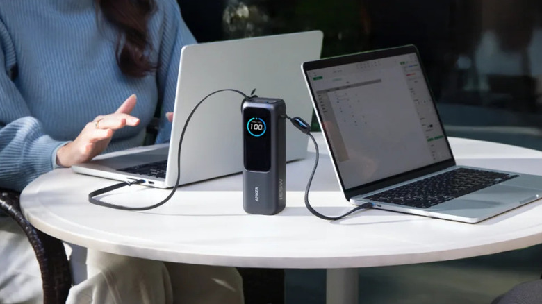 An Anker power bank on a coffee table with two laptops plugged into it.