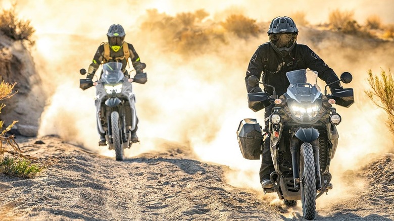 Two riders on a desert track riding Kawasaki KLR 650 motorcycles.