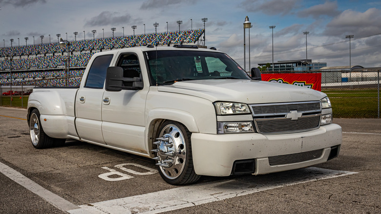 Front 3/4 view of a customized mid 2000s Chevy SIlverado HD dually pickup truck at race track.