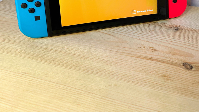 A Nintendo Switch with blue and red joycons in handheld mode showing an orange screen for the Nintendo eShop.