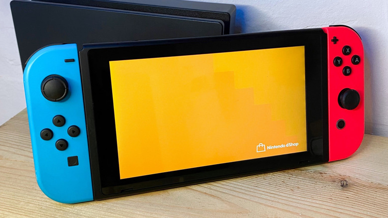 A Nintendo Switch with blue and red joycons in handheld mode showing an orange screen for the Nintendo eShop.