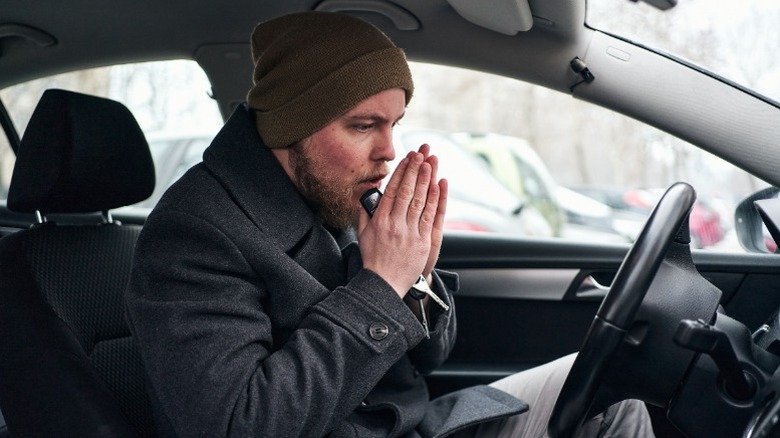 Man rubbing his hands to warm himself up in a car
