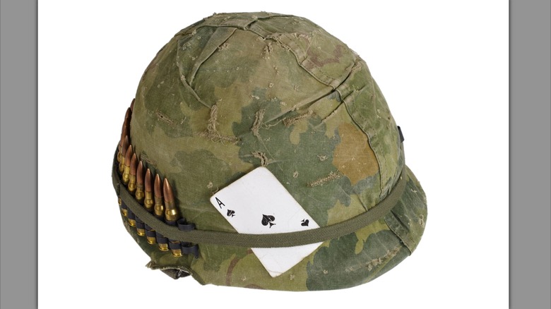US Army helmet from the Vietnam war period with camouflage cover and ammo belt and ace of spades playing card.