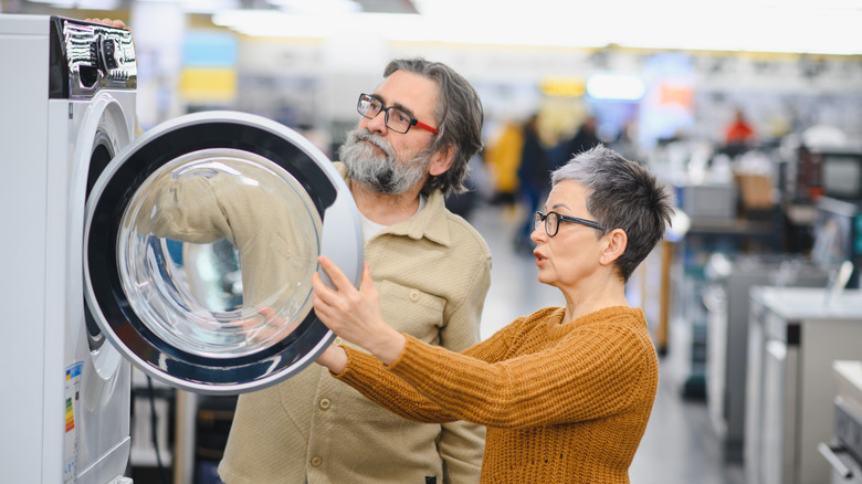 A couple inspecting a front load washing machine inside a large store