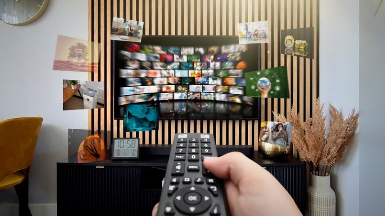 Person pointing a TV remote at a flatscreen TV surrounded by floating images.