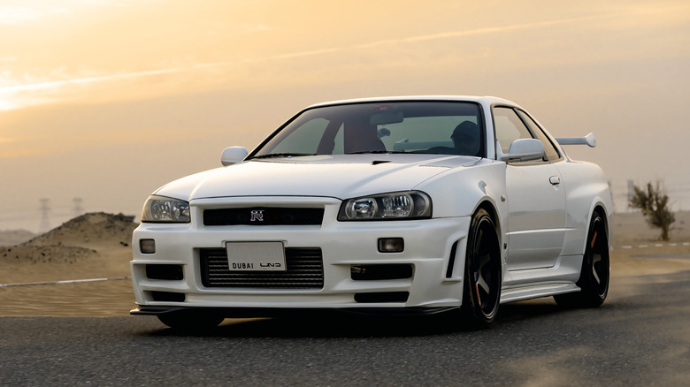 Nissan Skyline GT-R R34 V-Spec II showing front-end with bespoke hood fitted with NACA duct, parked against desert background, front-left view