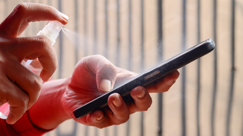 A person's hand spraying alcohol disinfectant on a mobile phone screen