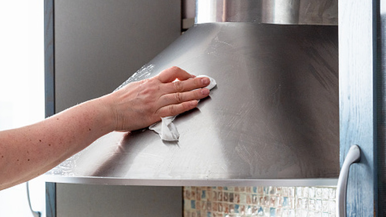 A person cleaning a stainless steel kitchen hood.