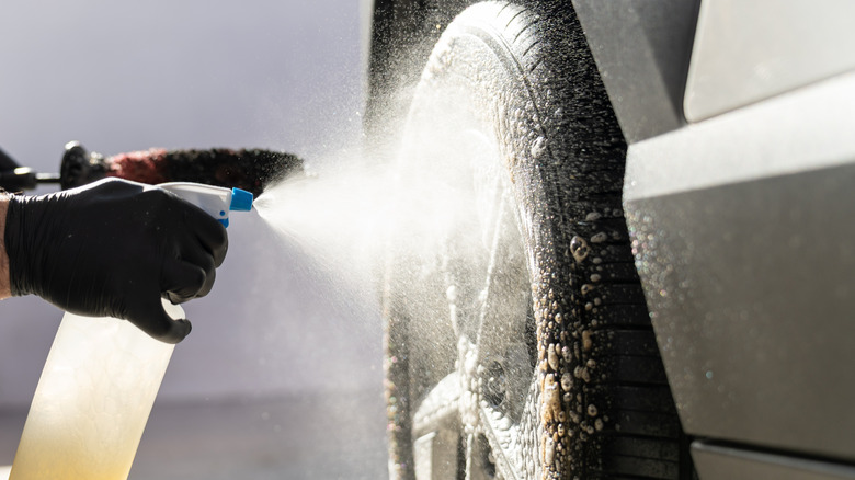 A close-up of person's gloved hands cleaning vehicle wheel and tires by spraying a cleaning solution