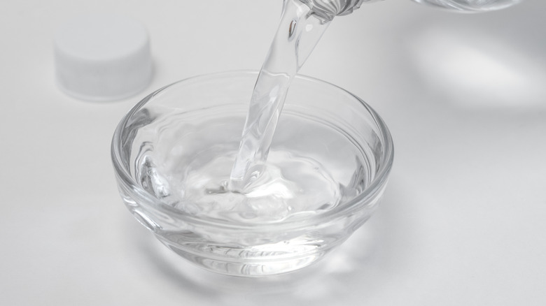 A hand pours white vinegar into a clear bowl