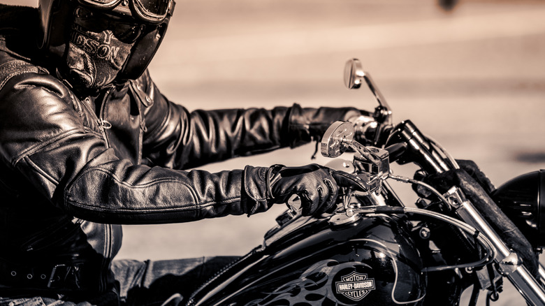A man wearing a leather jacket and a helmet riding a Harley-Davidson bike