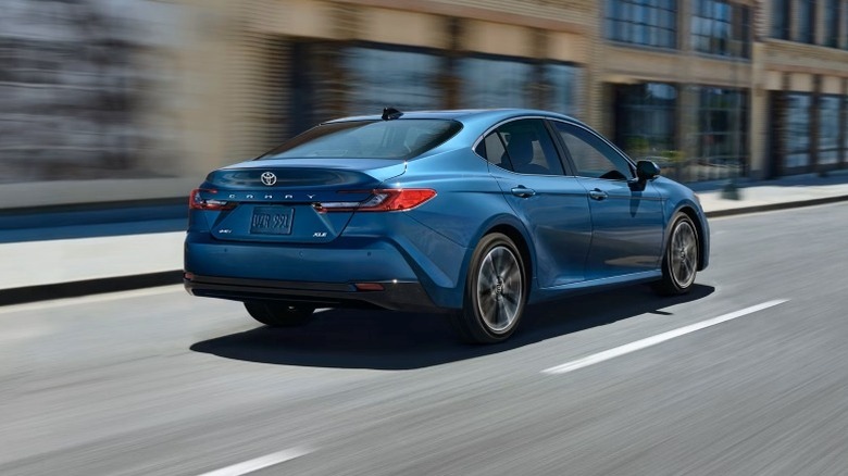Rear 3/4 shot of a 2025 Toyota Camry XLE driving down city street next to a building