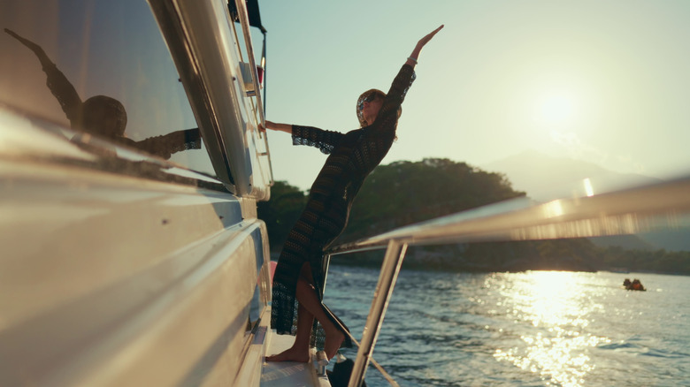 Woman stretches her arm to the sky while sailing on a yacht in the ocean at sunset.
