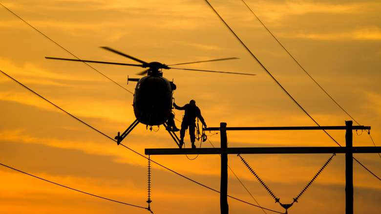 Front view of helicopter dropping off lineman on top of power lines at sunset.