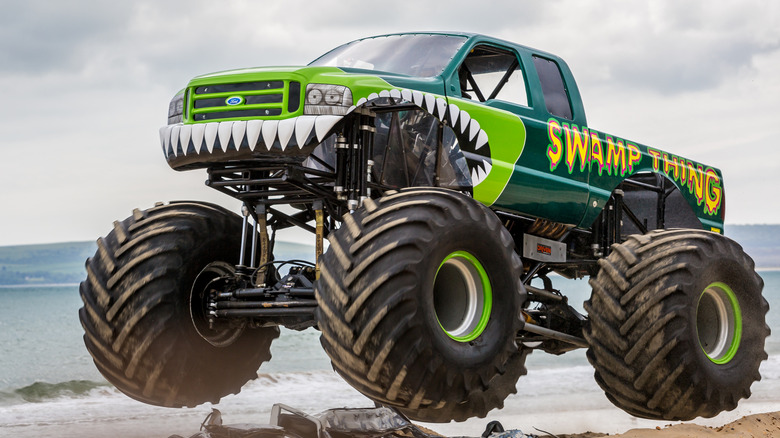 A green monster truck driving on a beach.